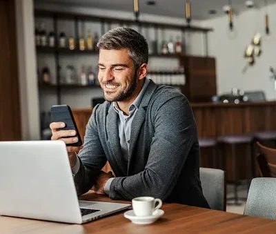 a happy businessman is sitting in a coffee shop and checking on his bank account on the