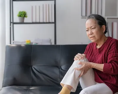 asian elderly woman sitting with knee pain on sofa at home